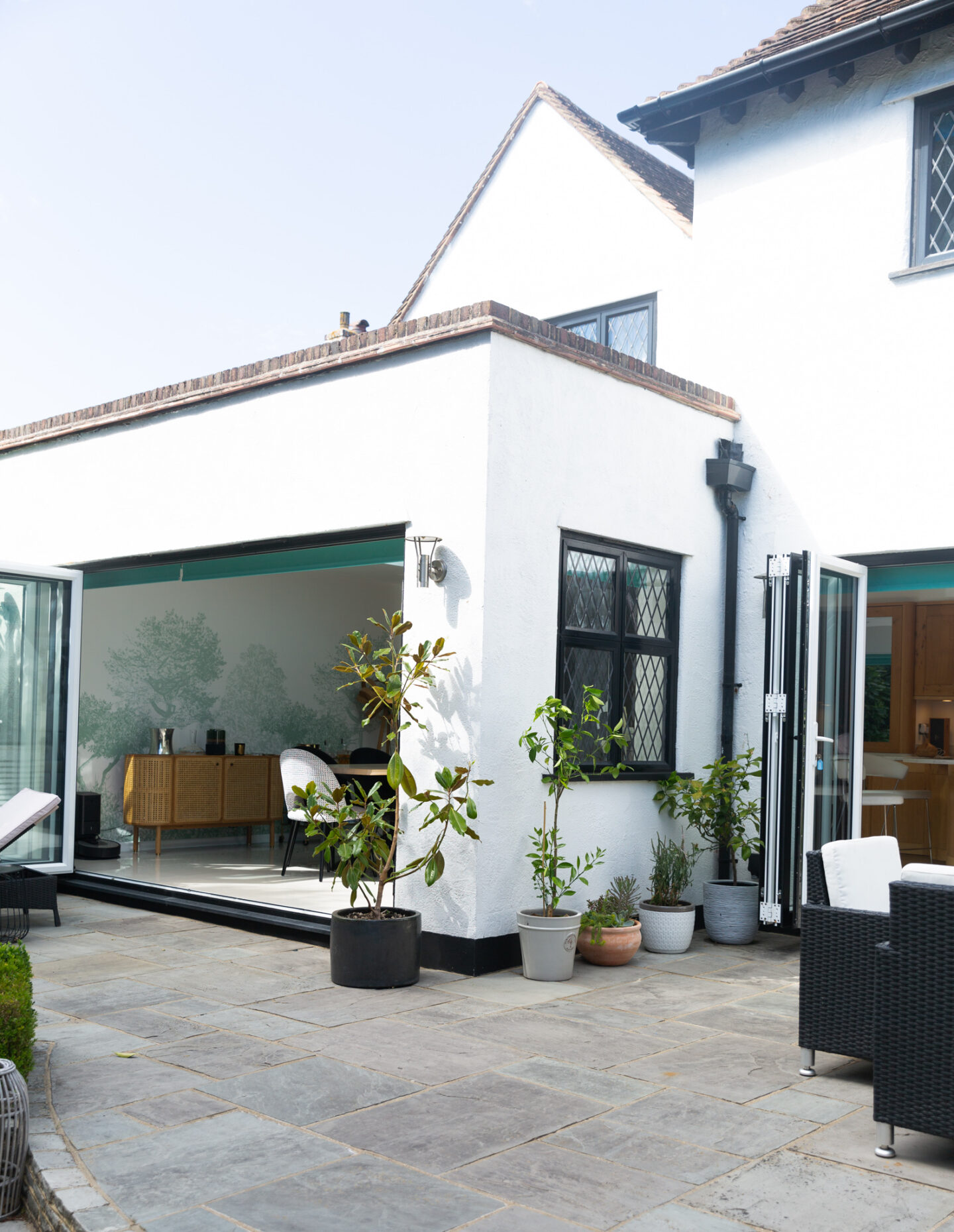 Paved garden patio with bi-fold doors and plants against the wall. 