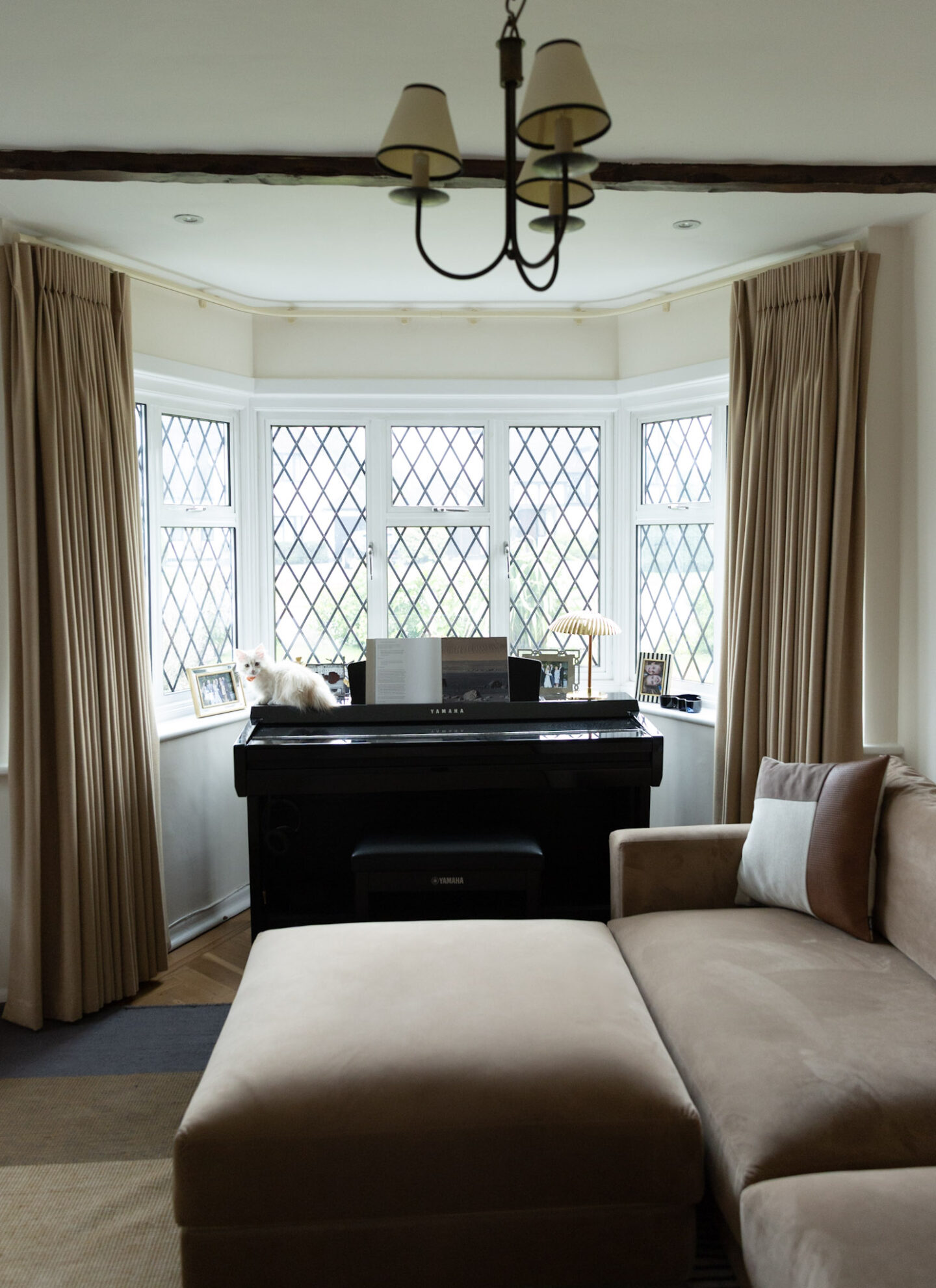 Full length beige curtains in bay window as part of living room transformation for uFurnish Home Awards 2026 with a white kitten on the piano