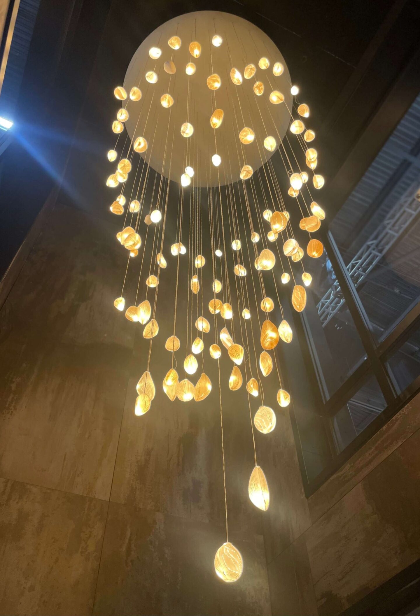 Large petal chandelier hanging next to a window.