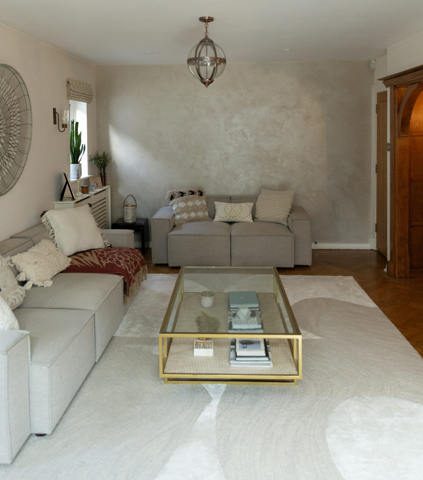 1920s period house living room with metallic plaster feature wall, large area abstract rug, two-tier glass coffee table and grey modular sofas 