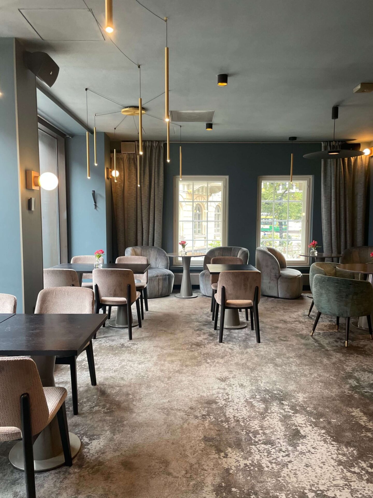 Contemporary brass pendant light hanging from a muted grey ceiling in a stylish hotel interior.