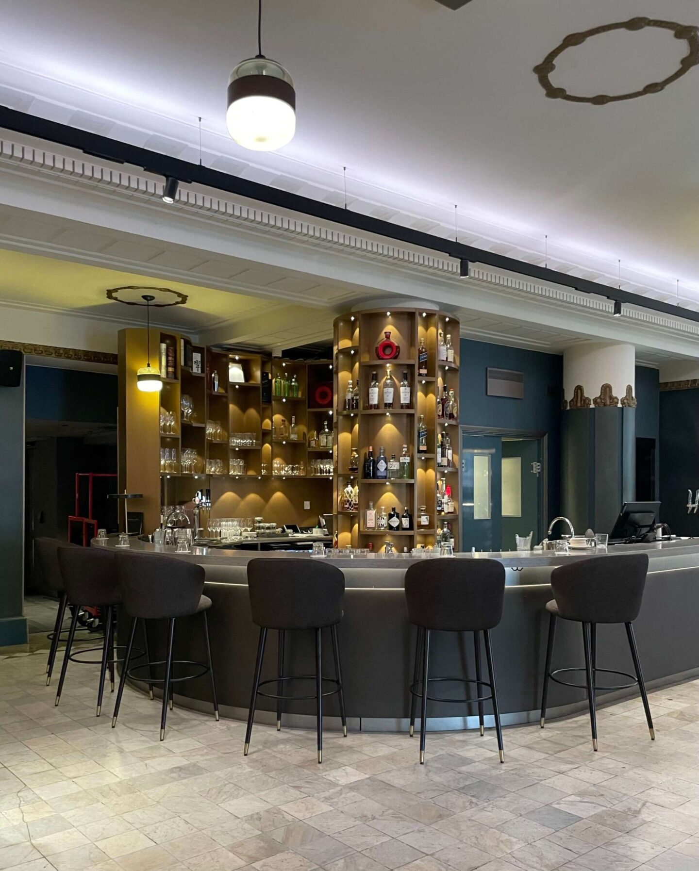Elegant hotel bar in the lobby with a round bar table and dark upholstered bar stools.